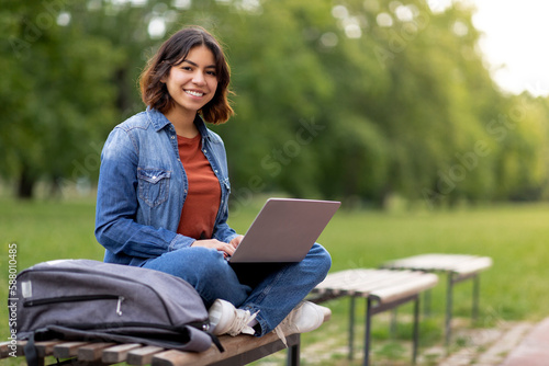 Beautiful Smiling Arab Female Student Using Laptop While Relaxing On Bench Outdoors