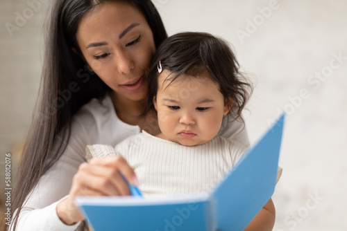 Korean Mommy And Infant Daughter Writing In Notebook At Home
