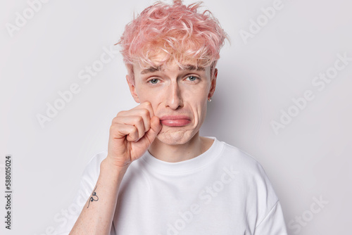 Sad frustrated adult man has doleful expression wipes tears found about something horrorful has troubles dressed in casual basic t shirt isolated over white background. Negative human emotions photo