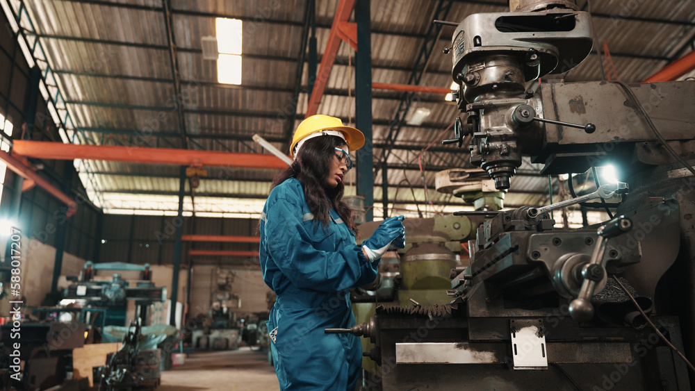 Two multiracial factory workers in safety wear are examining metal parts of machine together in metalwork production factory. Male and female production engineers are working on metal manufacturing. Two multiracial factory workers in safety wear are examining metal parts of machine together in metalwork production factory. Male and female production engineers are working on metal manufacturing.