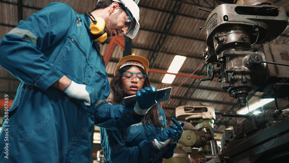 African factory worker in safety wear is checking a piece of industrial ...