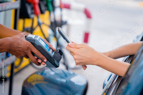 Woman using contactless payment by mobile phone with QR code at car filling station