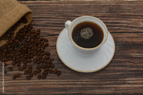 Grains of black coffee in a bag and a white cup with coffee. On a brown background.