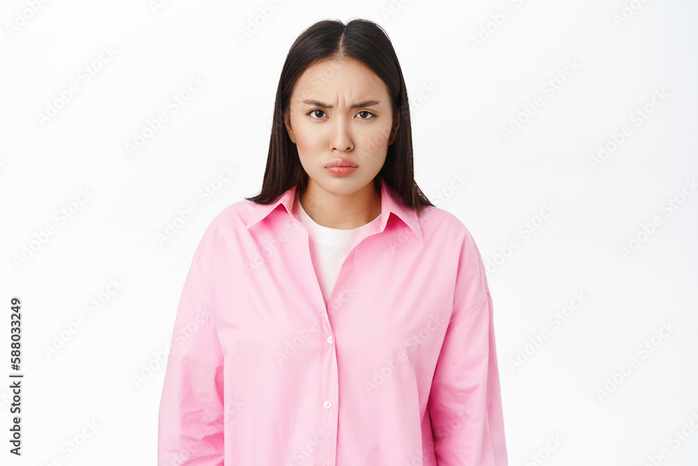 Portrait of angry asian girl frowns, looks offended at you, negative emotions, stands over white background Portrait of angry asian girl frowns, looks offended at you, negative emotions, stands over white background