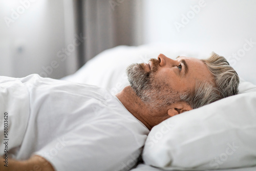 Unhappy frustrated middle aged man lying in bed