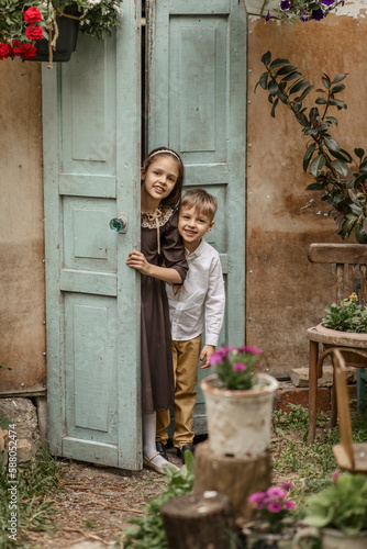kids, a girl and a boy, look out from behind a retro wooden door in a country house. the concept of country life in the village