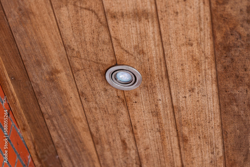 A portrait of a weather sealed light spot put in the wooden planks of a roof overhang. The lamp is turned off.
