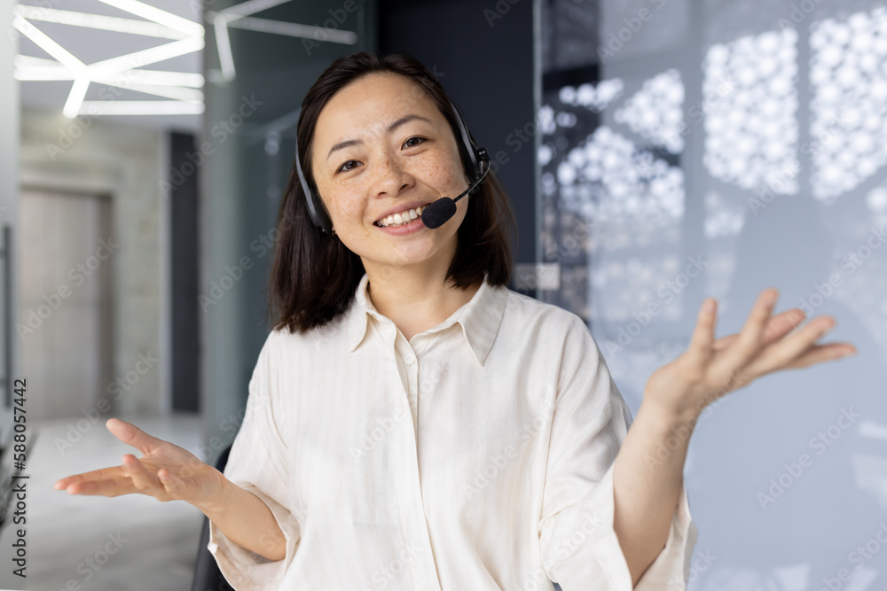 Businesswoman with video call headset smiling and looking at camera, Asian woman talking to customers remotely, tech support worker talking, webcam view