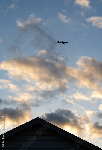 A portrait view of passenger jet in a sky at dusk flying over a house