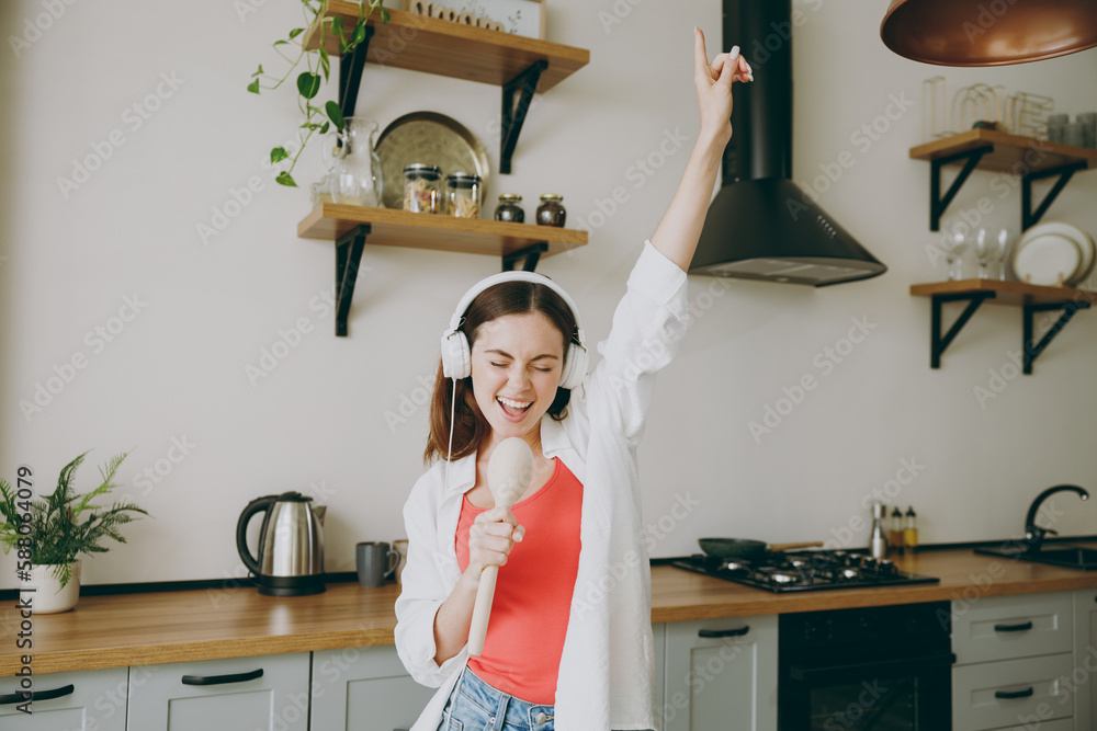 © ViDi Studio - Young cheerful singer fun positive caucasian housewife woman wearing casual clothes headphones listen music use spoon as microphone cooking food in light kitchen at home alone. Healthy diet concept. © ViDi Studio - Young cheerful singer fun positive caucasian housewife woman wearing casual clothes headphones listen music use spoon as microphone cooking food in light kitchen at home alone. Healthy diet concept.