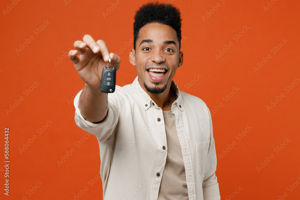Naklejka premium Young man of African American ethnicity wear light shirt casual clothes hold stretch handto camera with car keys fob keyless system do winner gesture isolated on orange red background studio portrait.