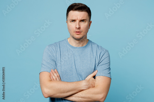 Young sad strict serious dissatisfied caucasian man wear casual t-shirt holding hands crossed folded look camera isolated on plain pastel light blue cyan background studio portrait. Lifestyle concept.