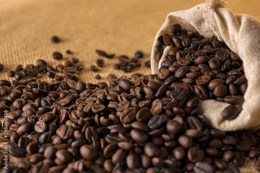 Heaps of roasted coffee beans in hemp bags and with seeds overflowing from the bag. Heaps of roasted coffee beans in hemp bags and with seeds overflowing from the bag.