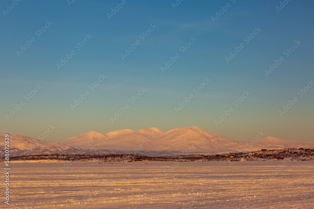 Abisko in Lapland in Sweden. Sunset at frozen Tornetrask Lake. Sun, snow, ice, the Arctic Circle, a landscape of northern Europe Abisko in Lapland in Sweden. Sunset at frozen Tornetrask Lake. Sun, snow, ice, the Arctic Circle, a landscape of northern Europe
