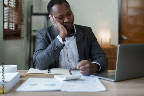Burnout American African business man in stress works with many paperwork document, migraine attack, Freelance, work from home
