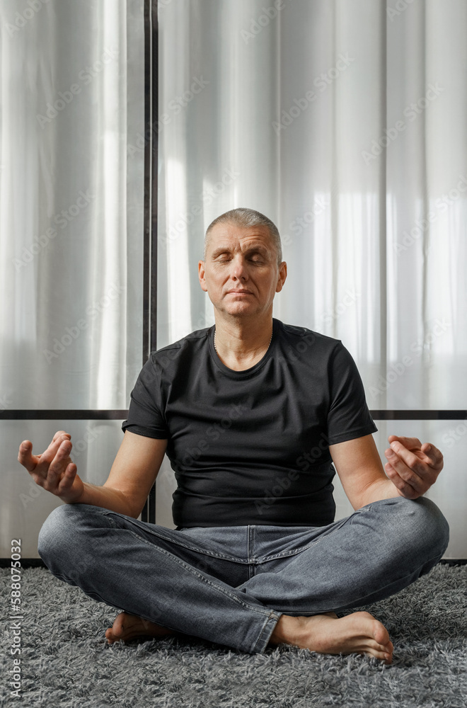 Fototapeta premium A man meditates in the lotus position on a yoga mat during a break from work.