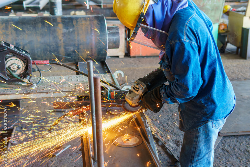 A worker uses Grinding Machine to grind the surface of the steel plate before assembling it into the steel pipe, at an Industrial factory. A worker uses Grinding Machine to grind the surface of the steel plate before assembling it into the steel pipe, at an Industrial factory.