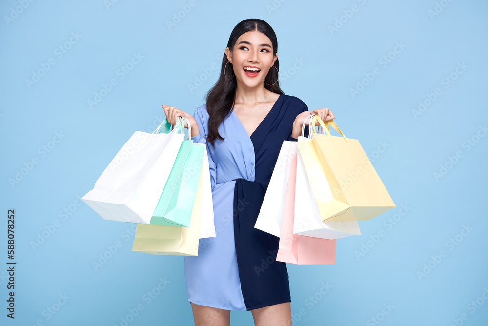 beautiful smiling Asian shopaholic woman holding shopping bags on blue studio background. beautiful smiling Asian shopaholic woman holding shopping bags on blue studio background.