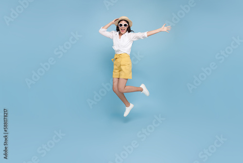 Happy smiling young Asian tourist woman jumping to summer time isolated on blue studio background. copy space