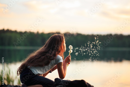 Pretty  little girl  is smiling in the park with dandelion flower. Happy cute kid having fun outdoors at sunset.
