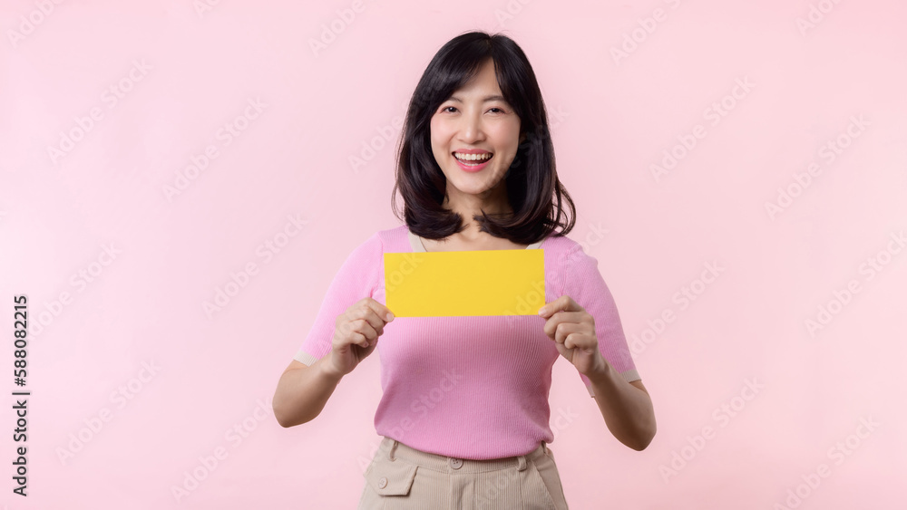 Portrait happy young woman model holding and showing blank space paper for advertisement information message poster with thumb up or point finger gesture isolated on pink pastel studio background. Portrait happy young woman model holding and showing blank space paper for advertisement information message poster with thumb up or point finger gesture isolated on pink pastel studio background.