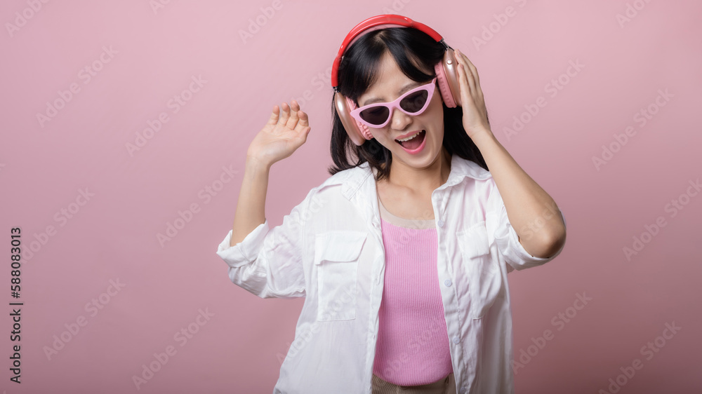 happy young asian woman model with stylish trendy sun glasses enjoy listening music by headphone audio and dancing isolated on pink studio background. technology, girl fashion, accessory concept. happy young asian woman model with stylish trendy sun glasses enjoy listening music by headphone audio and dancing isolated on pink studio background. technology, girl fashion, accessory concept.