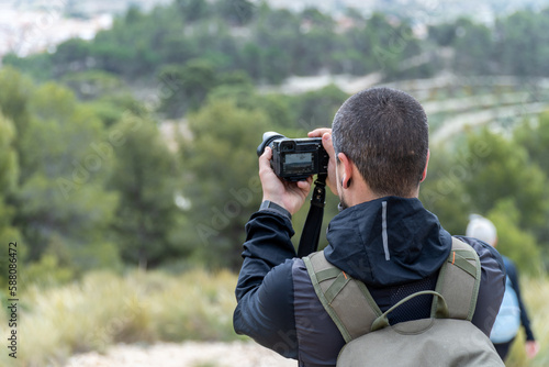 Young man with backpack taking photos outdoors 
