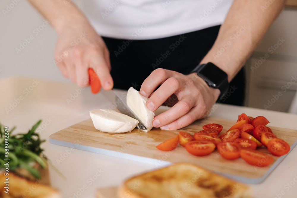 Man slice peace of mozzarella on wooden board. Preparing Italian classic sandwich