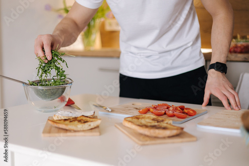 Fototapeta Naklejka Na Ścianę i Meble -  Close-up of man put organic arugula on bruschetta. Vegan food