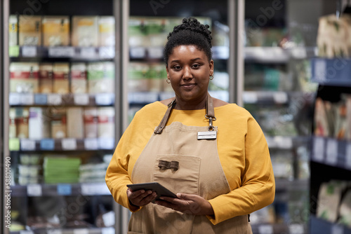 Waist up portrait of black female worker in supermarket smiling at camera, copy space