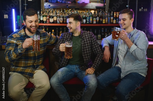 Old friends meeting. Happy young men in casual wear toasting with beer while sitting in beer pub together