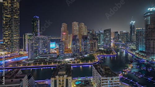 Panorama showing Dubai Marina with several boat and yachts parked in harbor and skyscrapers around canal aerial night timelapse.