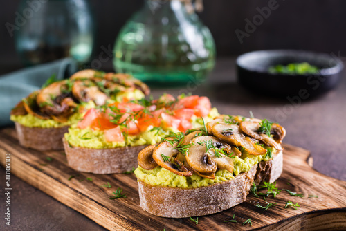 Sandwiches with avocado, fried champignons, tomatoes and herbs on rye bread on a board