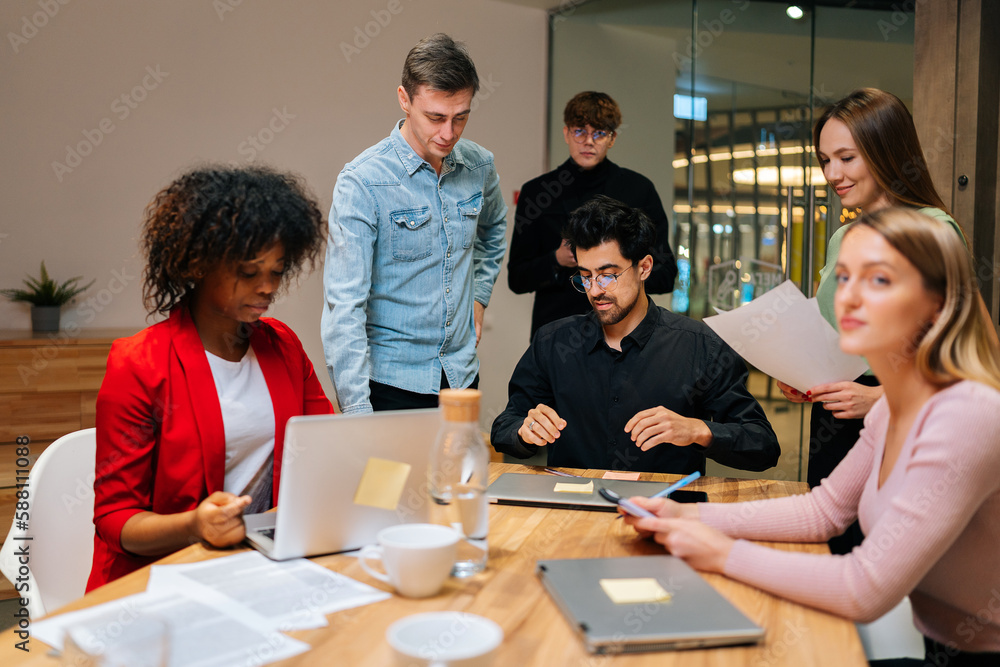 Portrait of multiethnic male and female colleagues working with project documents at meeting in boardroom, sitting at table, analyzing statistics, reading financial report, discussing strategy.