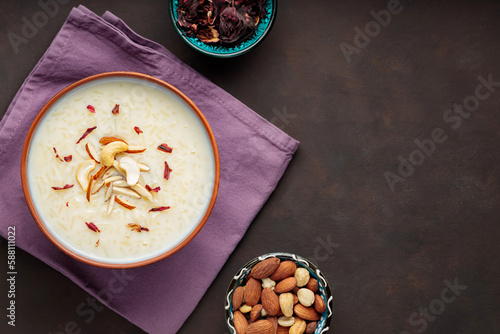 Rice kheer, nuts and dried hibiscus flowers on a dark background. Indian kheer rice pudding with nuts. Iftar muslim food concept. Top view photo