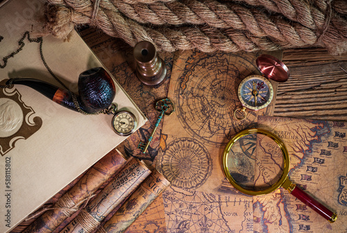 Old objects, book, magnifying glass, compass, pocket watch, spyglass, thick rope, tobacco pipe, old key lying on old maps in flat lay view