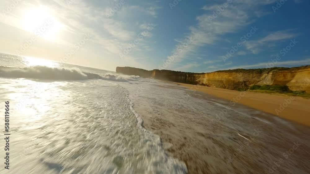 A drone flies along the ocean with waves at sunset next to a rock in Australia A drone flies along the ocean with waves at sunset next to a rock in Australia