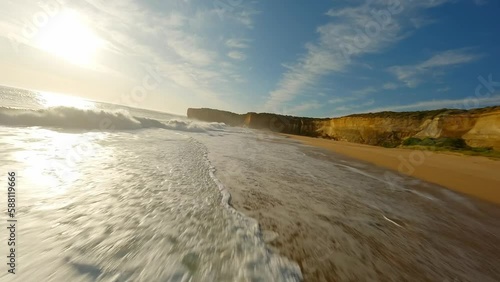 A drone flies along the ocean with waves at sunset next to a rock in Australia