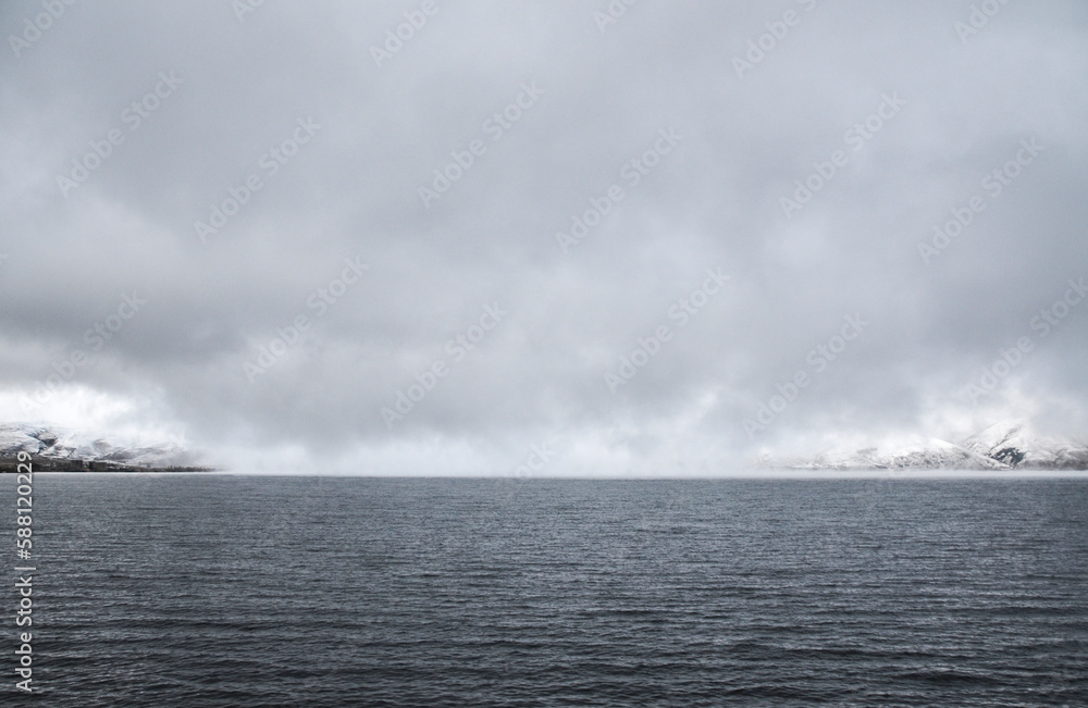 Gray water surface of Lake Sevan against the backdrop of snow-capped mountains under a stormy low sky. Armenia