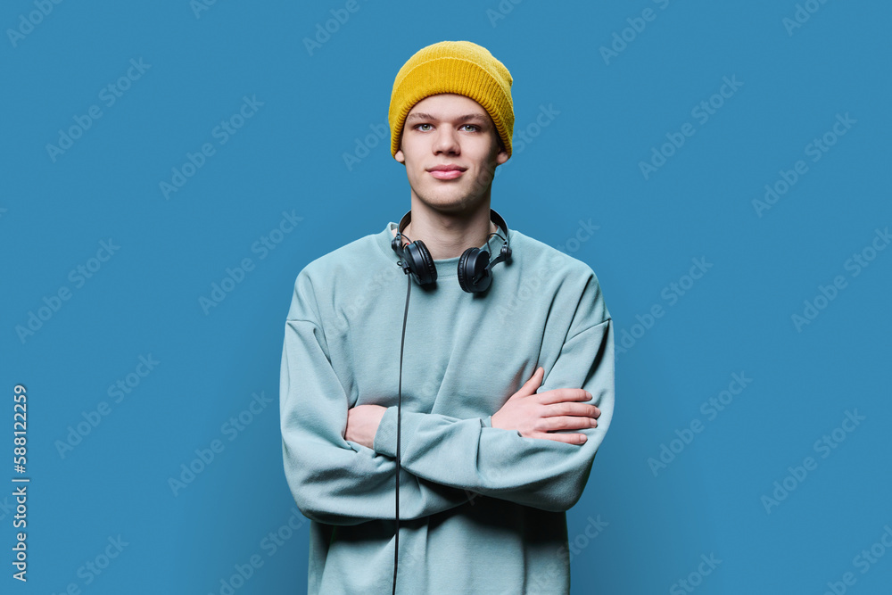 Young male in yellow cap sweatshirt with headphones on blue background Young male in yellow cap sweatshirt with headphones on blue background