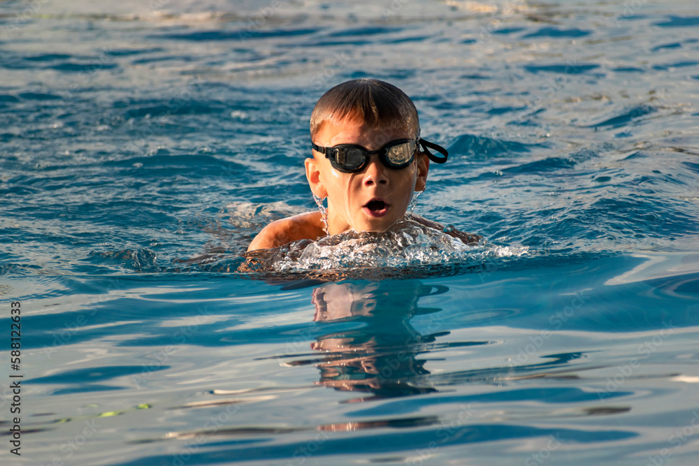 Portrait of boy child swimmer in outdoor swimming pool. Swim, water sports, training, competition, summer activities, healthy lifestyle, children's sport