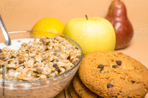 muesli in a glass bowl with milk, red pear, yellow apple, lemon, oatmeal cookies with chocolate