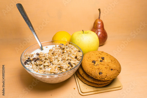 muesli in a glass bowl with milk, red pear, yellow apple, lemon, oatmeal cookies with chocolate