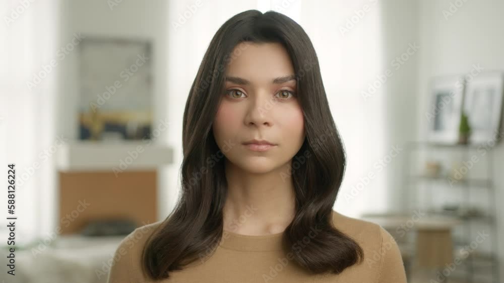 Zoom in portrait of young elegant woman looking up with serious confident face expression at camera in modern bright apartment with day light windows on background, slow motion real people 4K footage Zoom in portrait of young elegant woman looking up with serious confident face expression at camera in modern bright apartment with day light windows on background, slow motion real people 4K footage