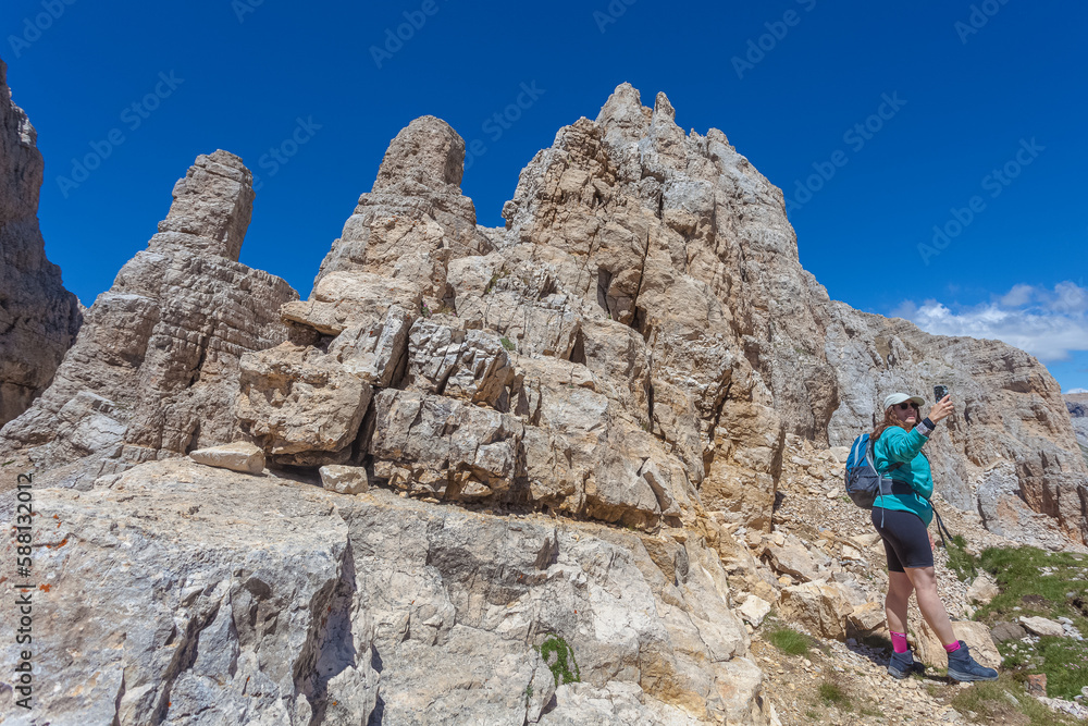 Girl with long air and cap taking photos with phone of dolomite peaks. Scenic landscape on the nature, Mount Latemar, Trentino, Italy. Traveling photography and outdoor sport activity concept