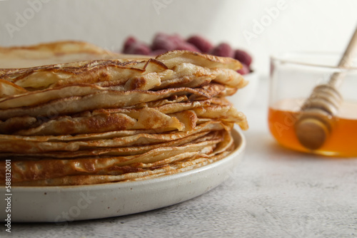 Stack of fresh crepes with honey and raspberries on the table copy space photo