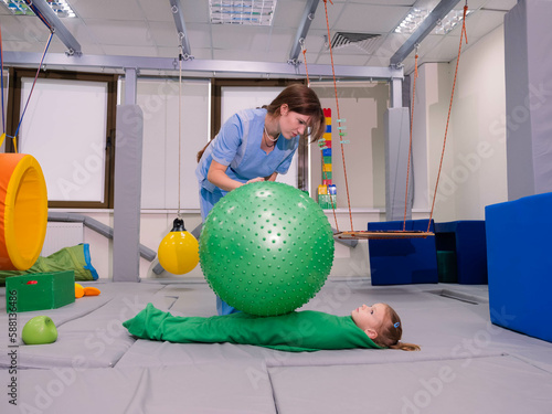 Physical therapist working with little girl in sensory room. Exercising with fitness ball and pressure to help kid relax in a therapy center. sensory integration session