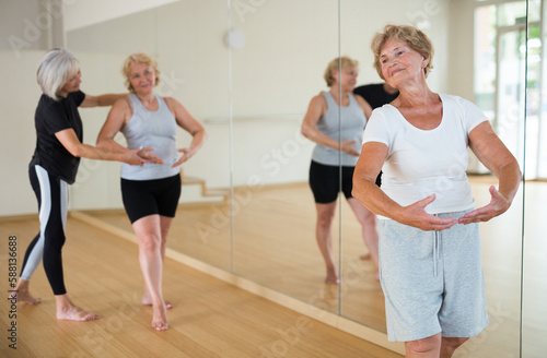 Elderly women who are engaged in the dance section at a group lesson stand in the 1st position of the ballet stand, where ..the choreographer helps them to do it correctly