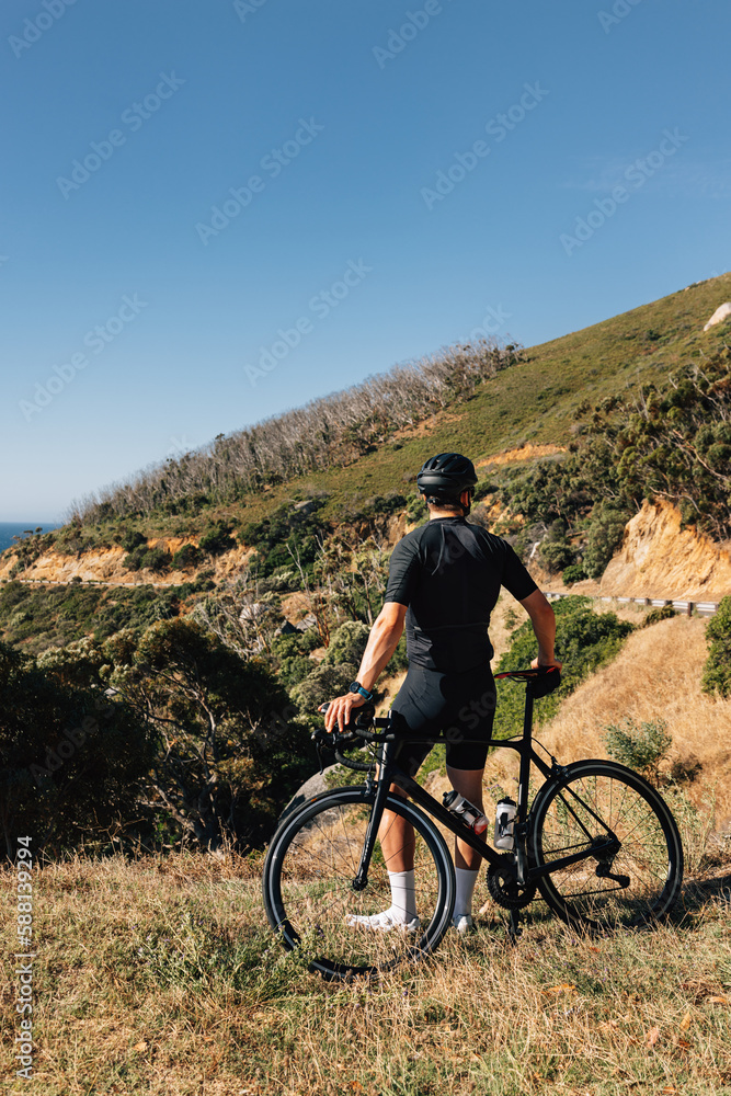 Professional cyclist in black sportswear leaning his bike looking at the view