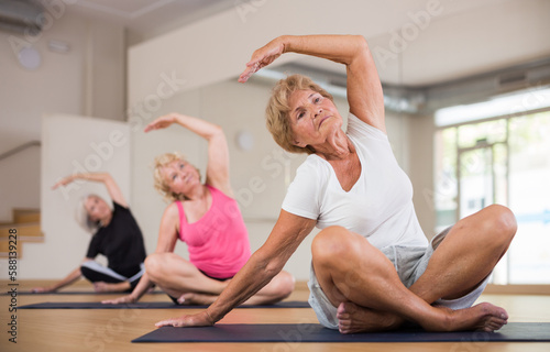 Elderly active women practicing yoga trainin the lotus position in the fitness studio during a group class